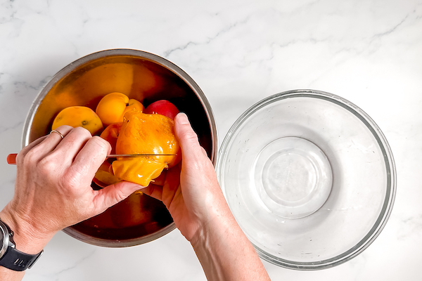 Using a knife to break the skin and pull it off the peach