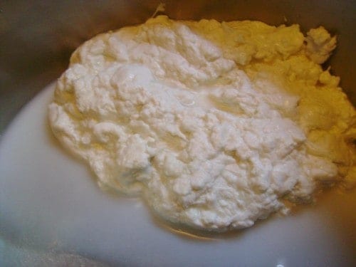 Image shows the mozzarella cheese starting to take shape, with curds forming and the whey in a pool to the side. 