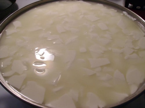 Image shows the metal vessel with the rennet and milk together, with large curds floating in it.