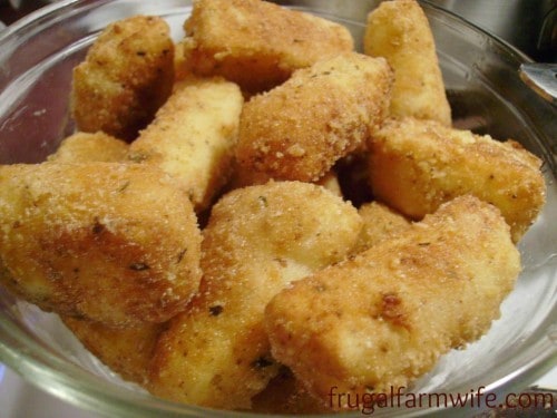Photo shows a close up of homemade, gluten free mozzarella sticks in a glass bowl. 