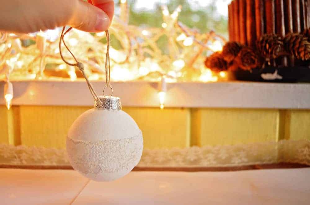 Image shows a hand holding the completed rustic lace ornament, with twine attached to hang it on the tree.