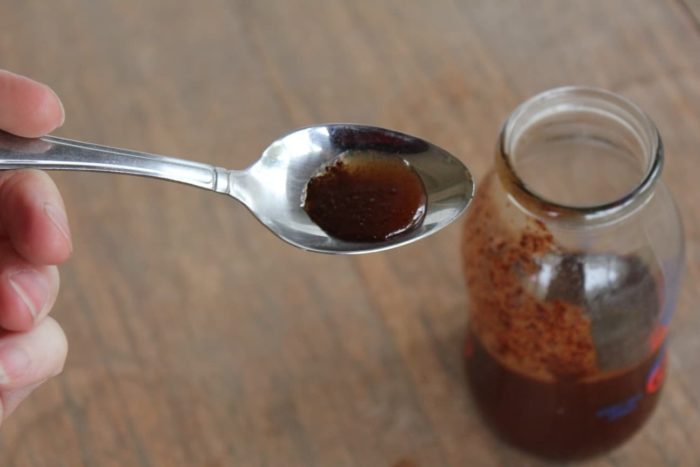 Photo shows a spoonful of syrup over a bottle