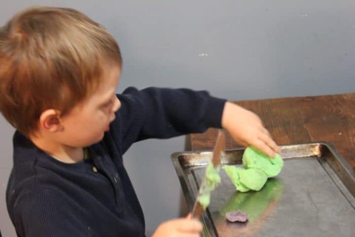 Photo shows a young child playing with play dough on a cookie sheet