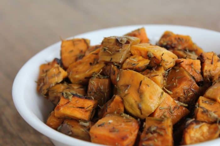 Image shows a white bowl full of roasted sweet potatoes