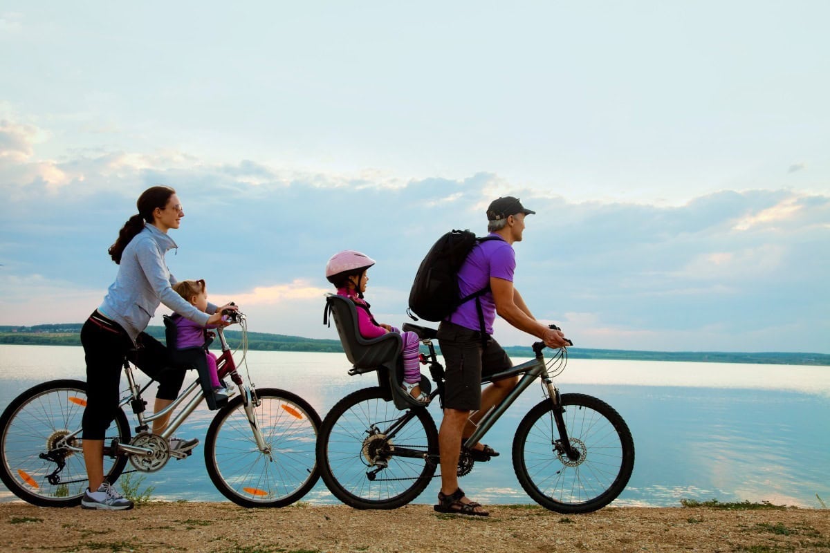 Image shows a family of four on bikes in front of a body of water. 