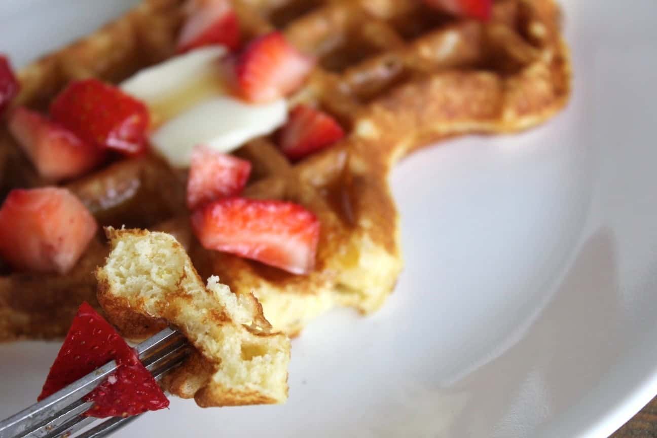 Image shows a bite of waffle on a fork over a plate.
