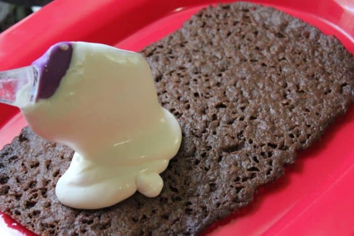 Photo shows a spatula spreading the ice cream over the cookie on a red platter