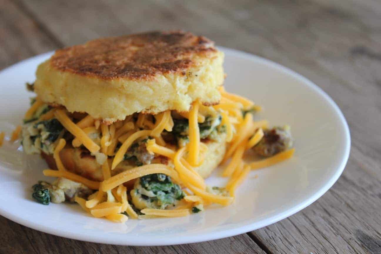Image shows a gluten free English muffin made into an egg and spinach sandwich on a white plate. 