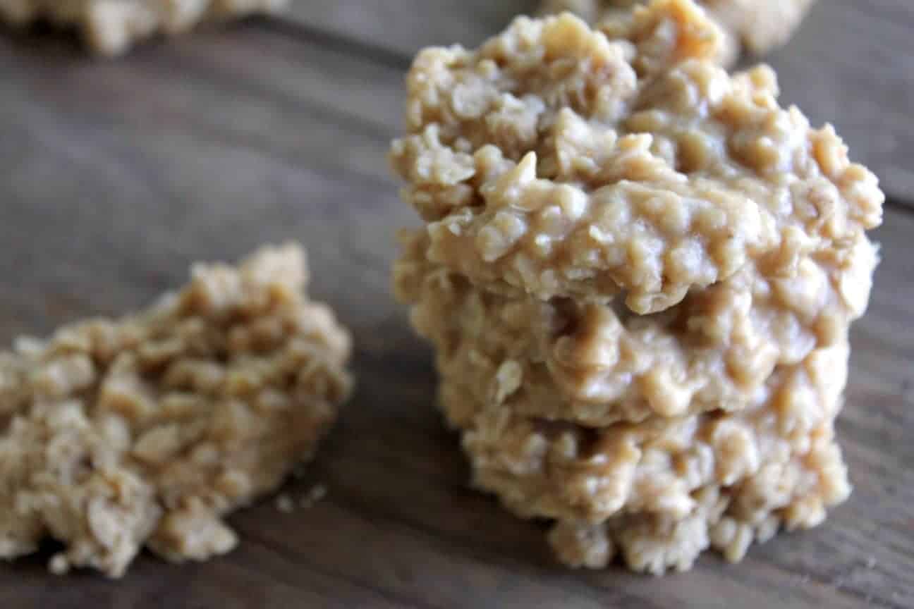 Photo shows a small stack of peanut butter no bake cookies on a brown table. Another cookie sits next to the stack.