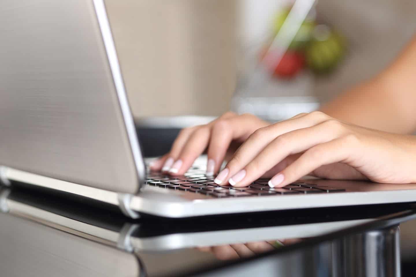 Image shows hands typing on a laptop computer on a shiny table