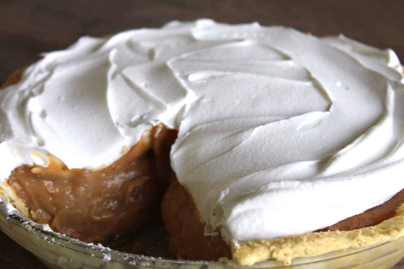 Image shows a pumpkin cream pie in a pie dish, with whipped cream on top. One slice is missing from the pie.