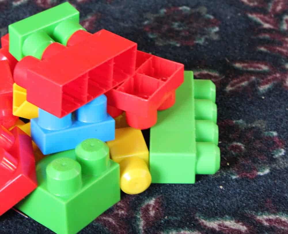 Image shows a pile of large toy blocks on a dark colored carpet. 