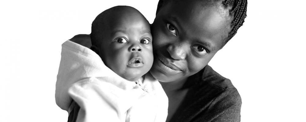 Image shows a woman holding a small baby in a hooded onesie. Both are looking at the camera.