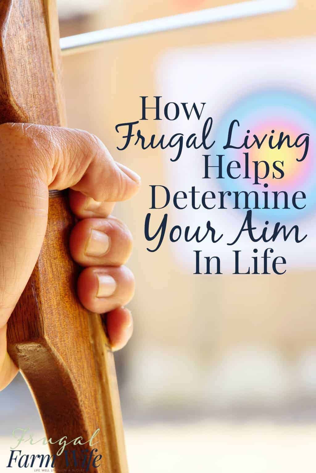 Image shows a hand holding a bow, with a blurry target in the background. Text reads "How Frugal Living Helps Determine Your Aim in Life"