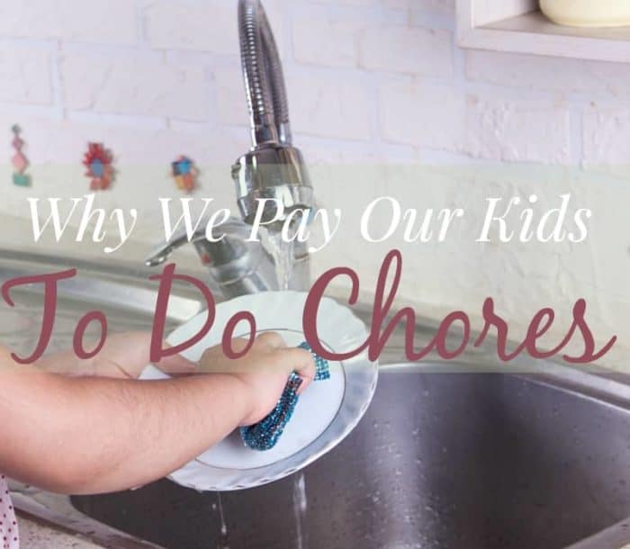 Image shows the arms of a young child holding a dish over a sink to wash it. Text reads "Why We Pay Our Kids to do Chores"