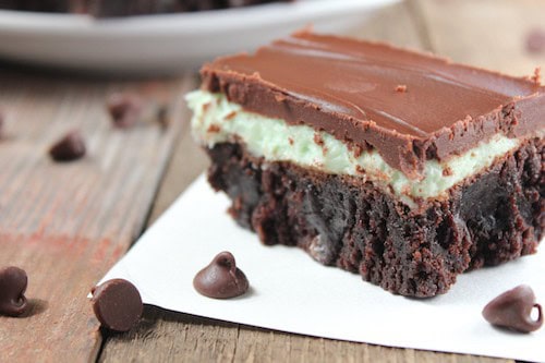 Image shows a close up of a chocolate and peppermint brownie on a table with chocolate chips scattered nearby.