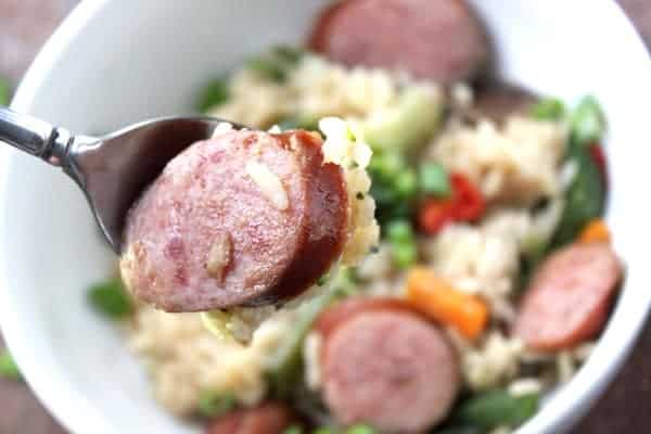Image shows a close up of a spoon holding a piece of sausage, over a bowl of Asian Sausage Casserole