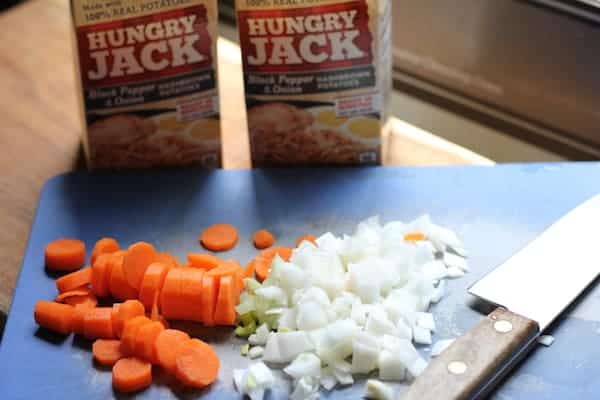 Photo shows a cutting board with carrots and onions sliced with a knife