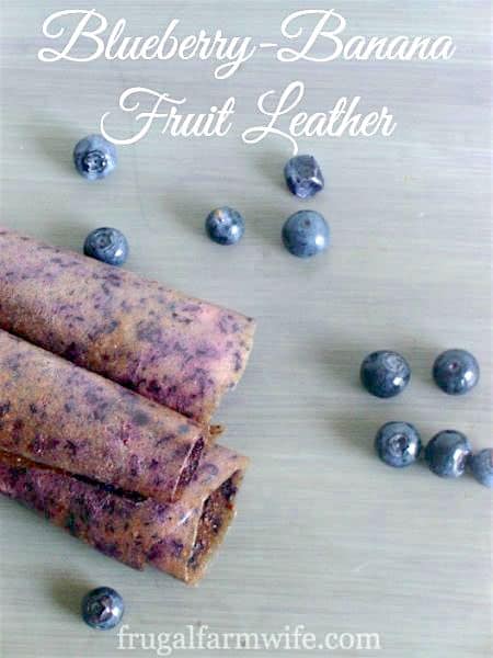 Image shows several pieces of fruit leather rolled on a table with text that reads "Blueberry-Banana Fruit Leather"