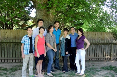 Image shows a group of siblings standing under a tree in front of a fence. 