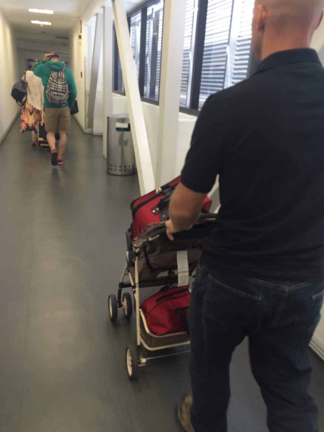 Image shows a man pushing a stroller through an airport, following other passengers with luggage and bags.