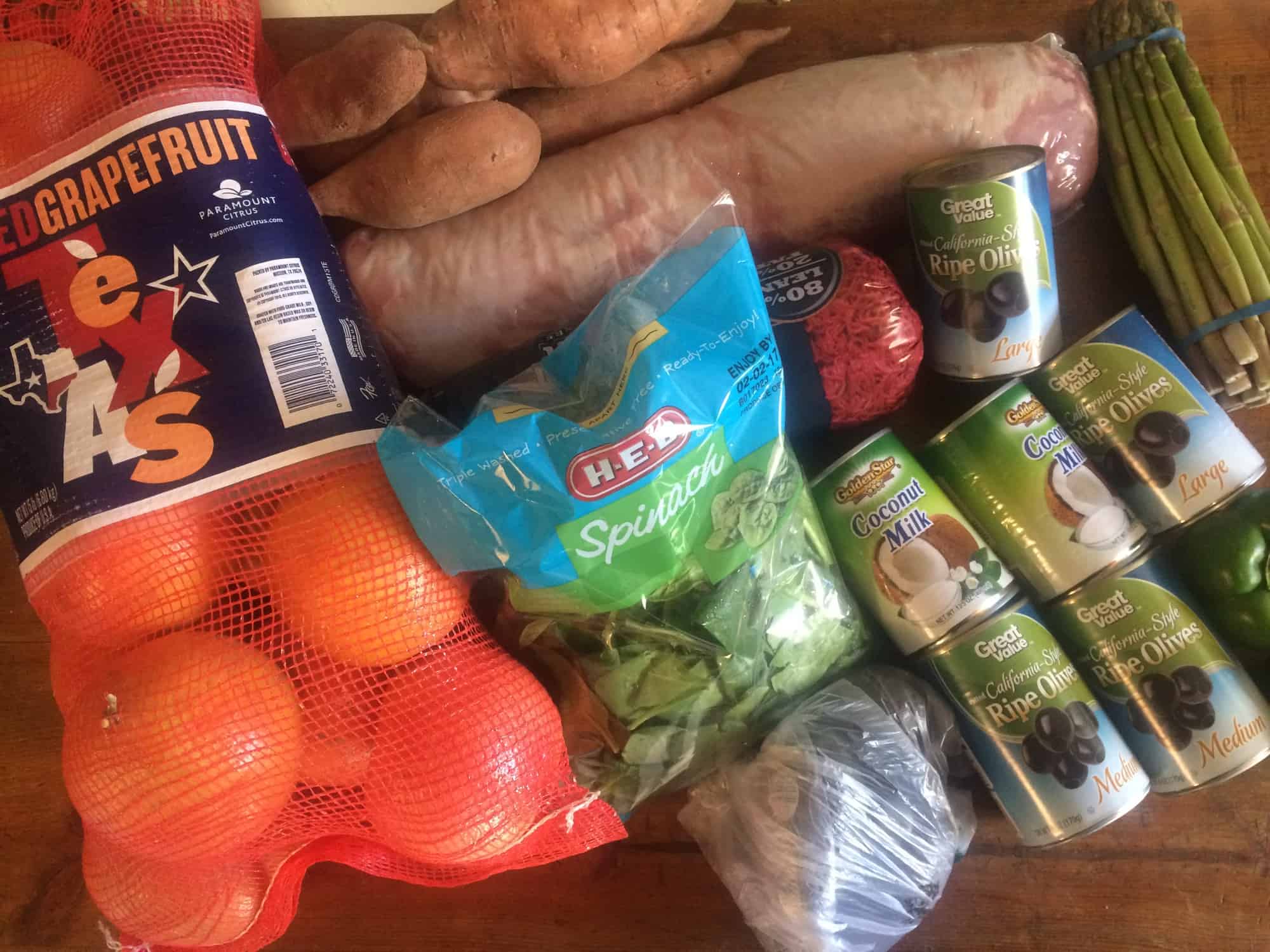 Image shows a table full of groceries for Whole 30 week 1- grapefruit, spinach, asparagus, olives, coconut milk and more