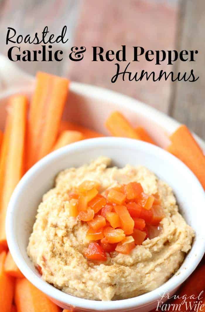 Image shows a close up of a bowl of hummus, surrounded by carrots. Text overlay reads "roasted garlic and red pepper hummus"