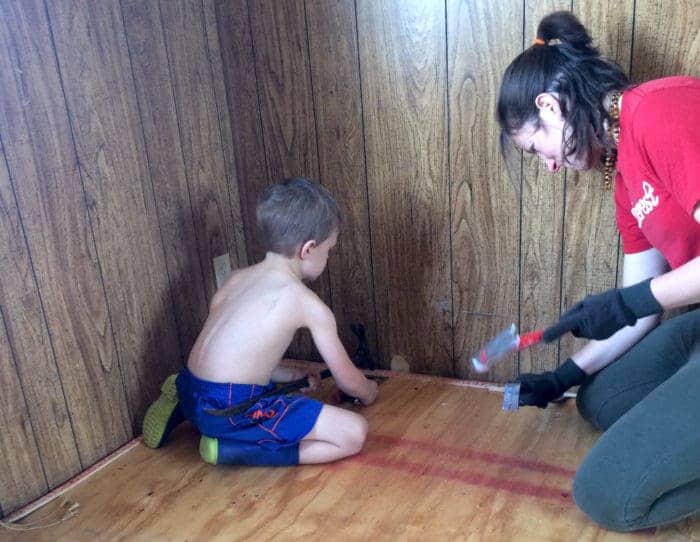 Photo shows a young boy and woman hammering the wood floor of a mobile home