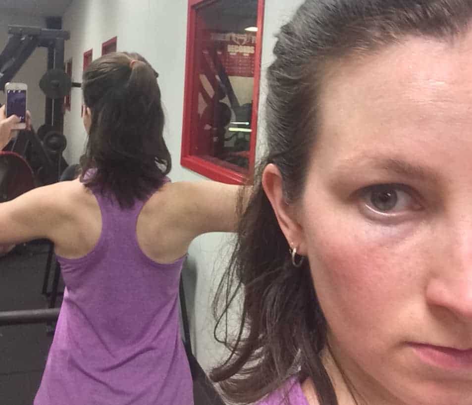 Image shows a woman taking a photo of her back in a mirror at a gym.