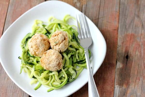 Image shows a white plate with zucchini noodles on it. Three tuna balls sit on top of the zoodles, and a fork rests on the plate with them. 