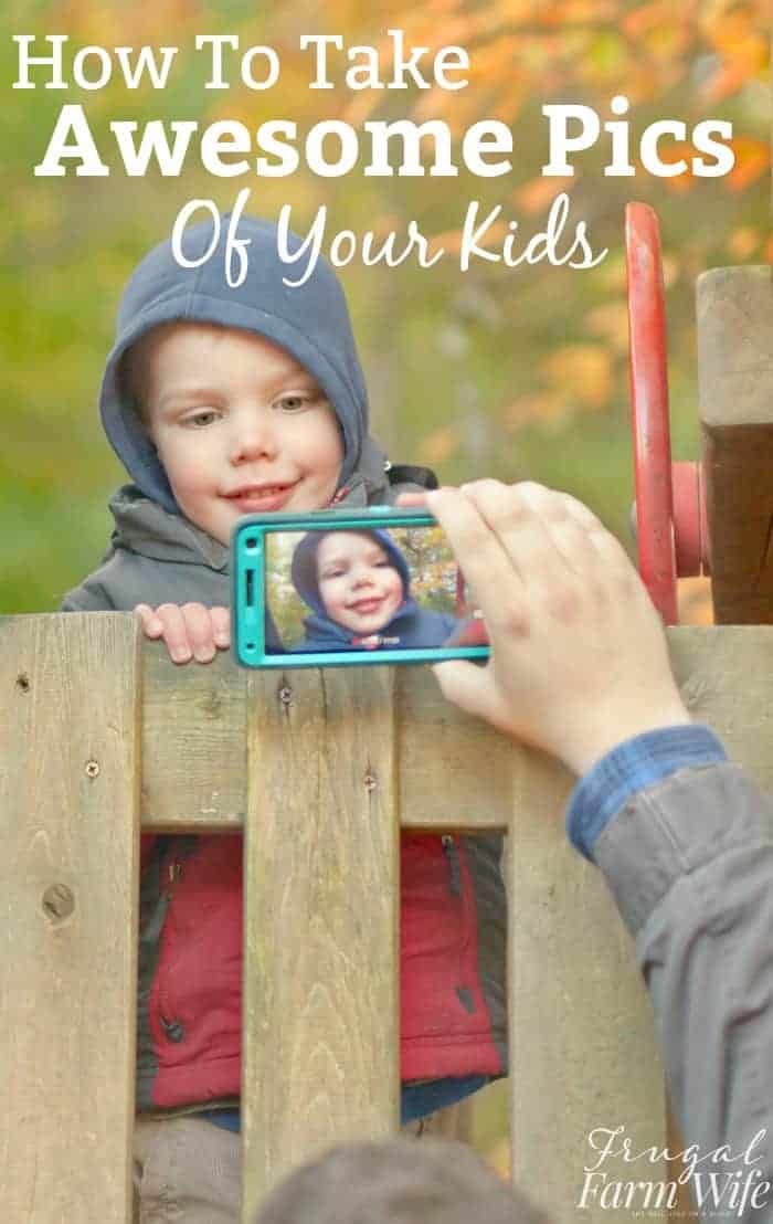 Image shows a small child peeking over a fence in a hooded sweatshirt, with a camera phone snapping his photo. Text above reads "How to Take Awesome Pics of Your Kids"