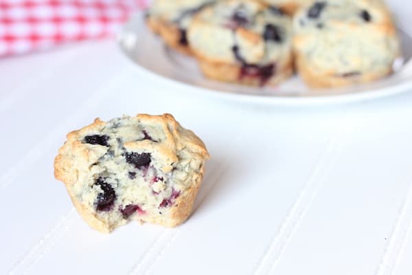 Image shows a blueberry muffin on a table next to a plate of muffins