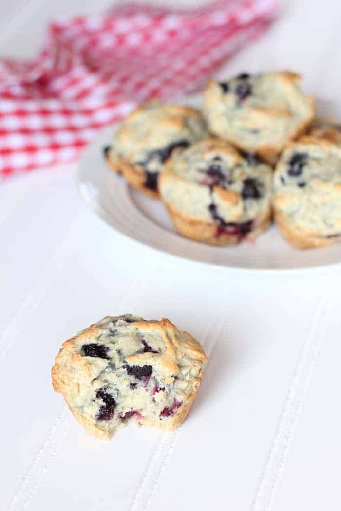 Image shows a plate of blueberry muffins  with one sitting next to it