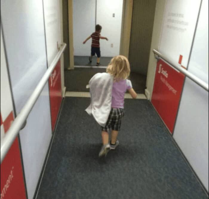 Image shows  the backs of two small children running down the jetway to an airplane.