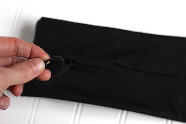 Image shows a black running belt on a white table, with a hand holding the small clasp at the zipper.