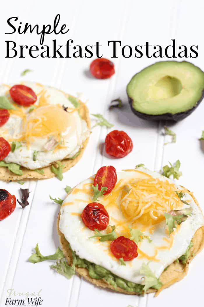 Image shows two simple breakfast tostadas topped with egg, cheese, avocado and tomato on a counter. Text overlay reads "Simple Breakfast Tostadas"