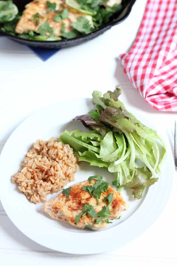Image shows a plate with a serving of chicken, rice and greens on a table. 