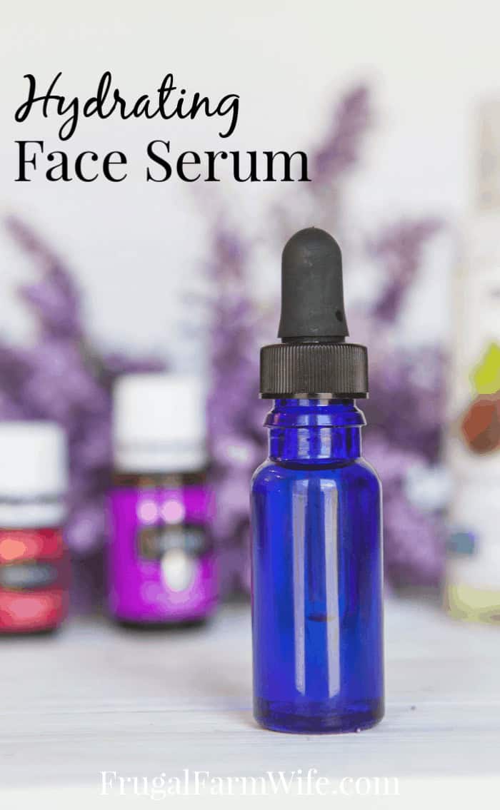 Image shows a close up of a blue dropper bottle on a table. Several bottles of essential oils are blurred in the background. Text above reads "Hydrating Face Serum"