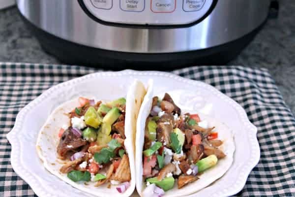 Image shows two pulled pork tacos on a plate in front of an Instant Pot