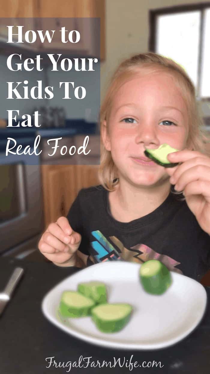 Image shows a young child looking at the camera holding a piece of zucchini. Text overlay reads "How to Get Your Kids to Eat Real Food"