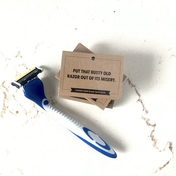Image shows a razor from Dollar Shave Club on a counter top with a small stack of extra razors next to it. 