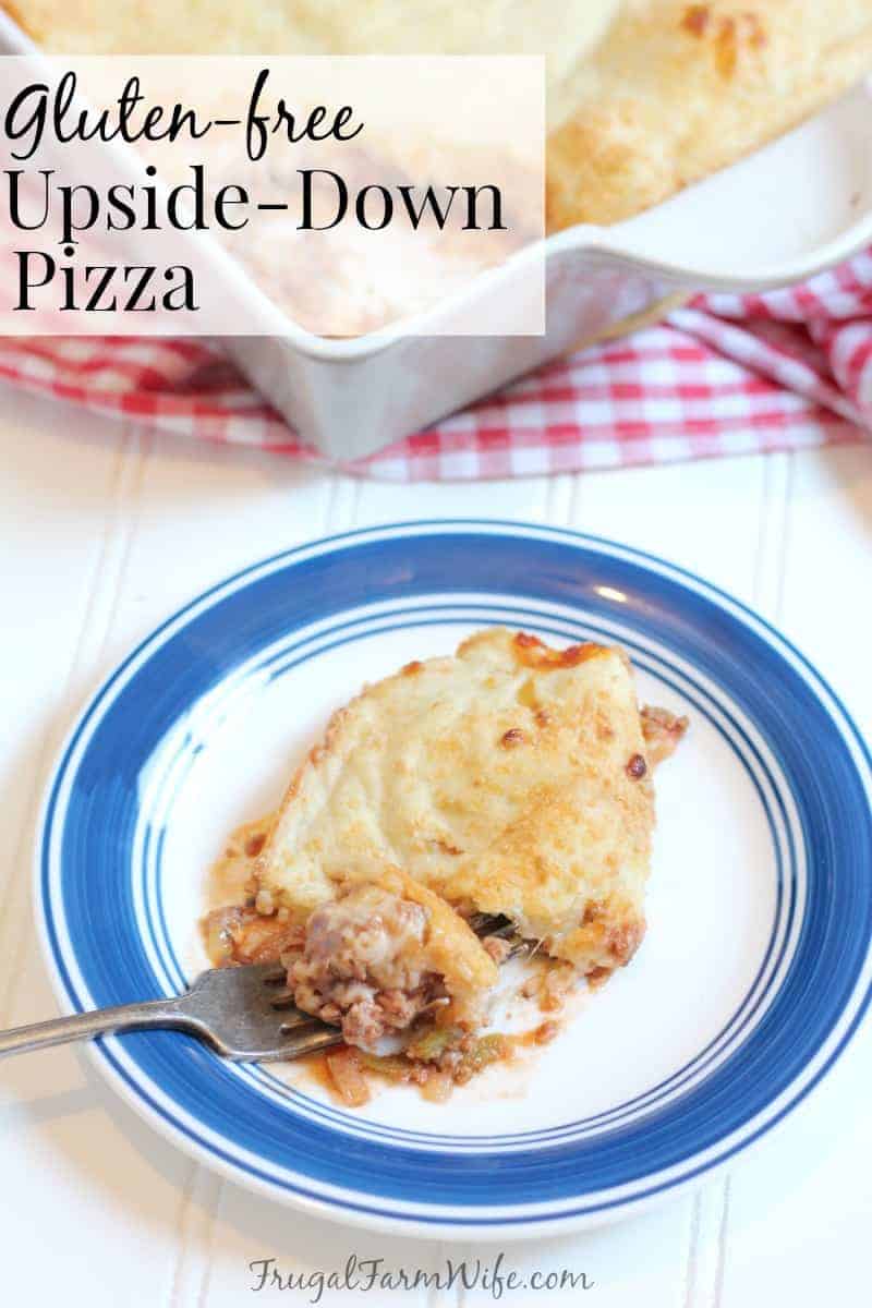 Image shows a white plate with blue trim with a piece of gluten-free upside-down pizza on it with a fork taking a bite. Behind the plate is a red and white checked tablecloth with more casserole sitting on top. Text overlay reads "Gluten-free Upside-down pizza"