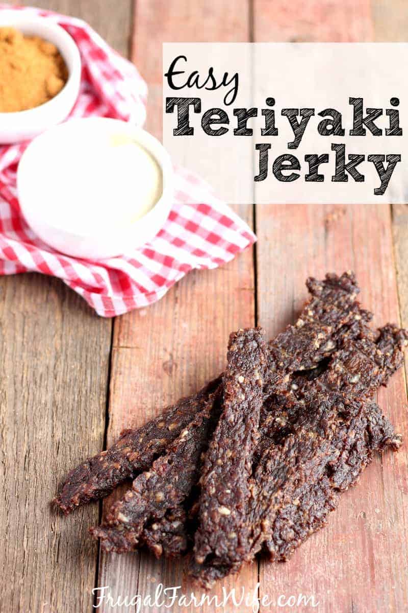 Image shows several pieces of teriyaki venison jerky on a table, with two small dishes of sauce nearby. Text overlay reads "Easy Teriyaki Jerky"