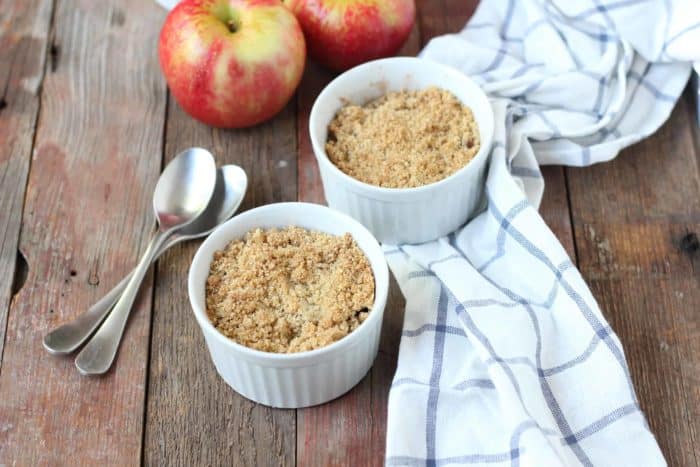 Image shows two bowls of apple crisp, with spoons, two apples and a napkin