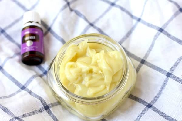 Photo shows a jar of body butter on a cloth, next to a small jar of essential oils