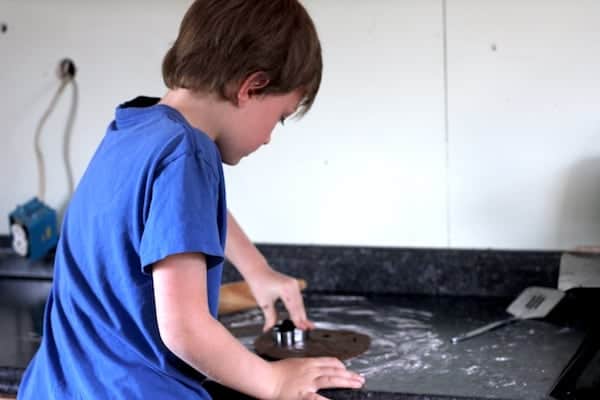 Image shows a young boy cutting gingerbread men out with a cookie cutter