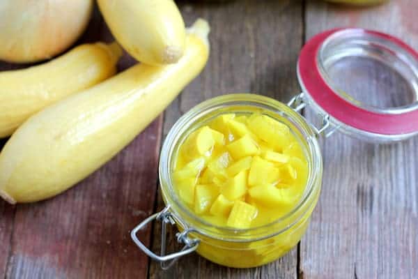 Image shows several summer squash sitting next to an open jar of summer squash pickles