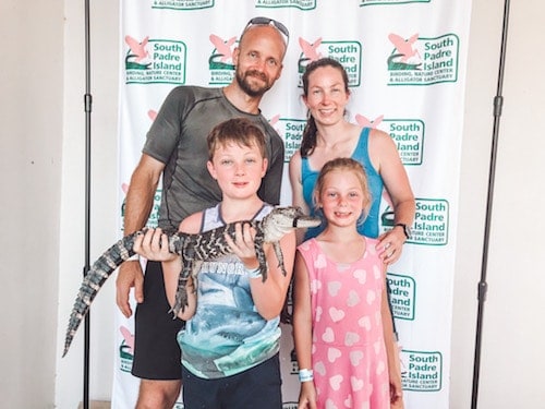 Photo shows a family posing with a boy holding a small alligator