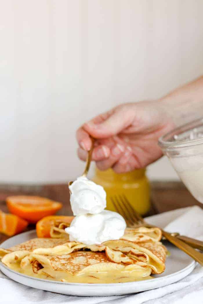 Image shows a hand placing dollops of orange curd on crepes