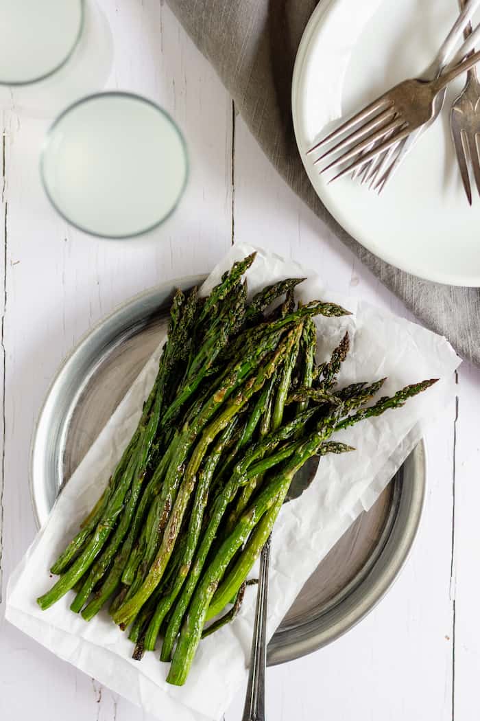 Image shows a plate of oven roasted asparagus next to an empty plate of silverware